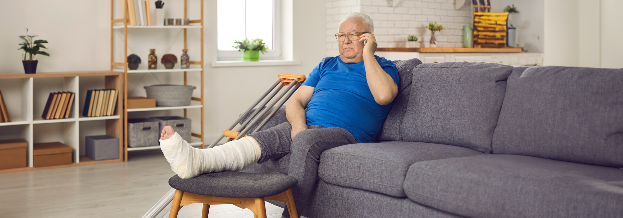 senior man with broken leg in plaster cast sitting on sofa and making phone call